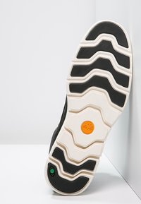 Svart gummisula med ett vågigt mönster, med vita accenter och en orange trälogo. Strukturerad yta för grepp och hållbarhet.