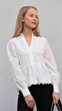 Balta siuvinėta bluzonė su aklomis ornamentais, V formos iškirpte, ilgesnėmis pūstomis rankovėmis ir banguotu apvadu, derinama su juodomis kelnėmis ir krepšiu.