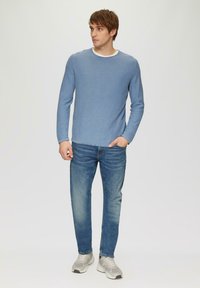 Helleblaues Langarmhemd mit Rundhalsausschnitt, kombiniert mit mittelblauen Jeans und grauen Sneakers. Einfaches Design, minimale Details.