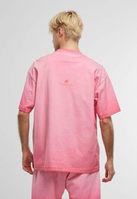 Tricou din bumbac roz cu o croială lejeră, mâneci scurte și guler rotund, având un imprimeu subtil pe partea superioară a spatelui.