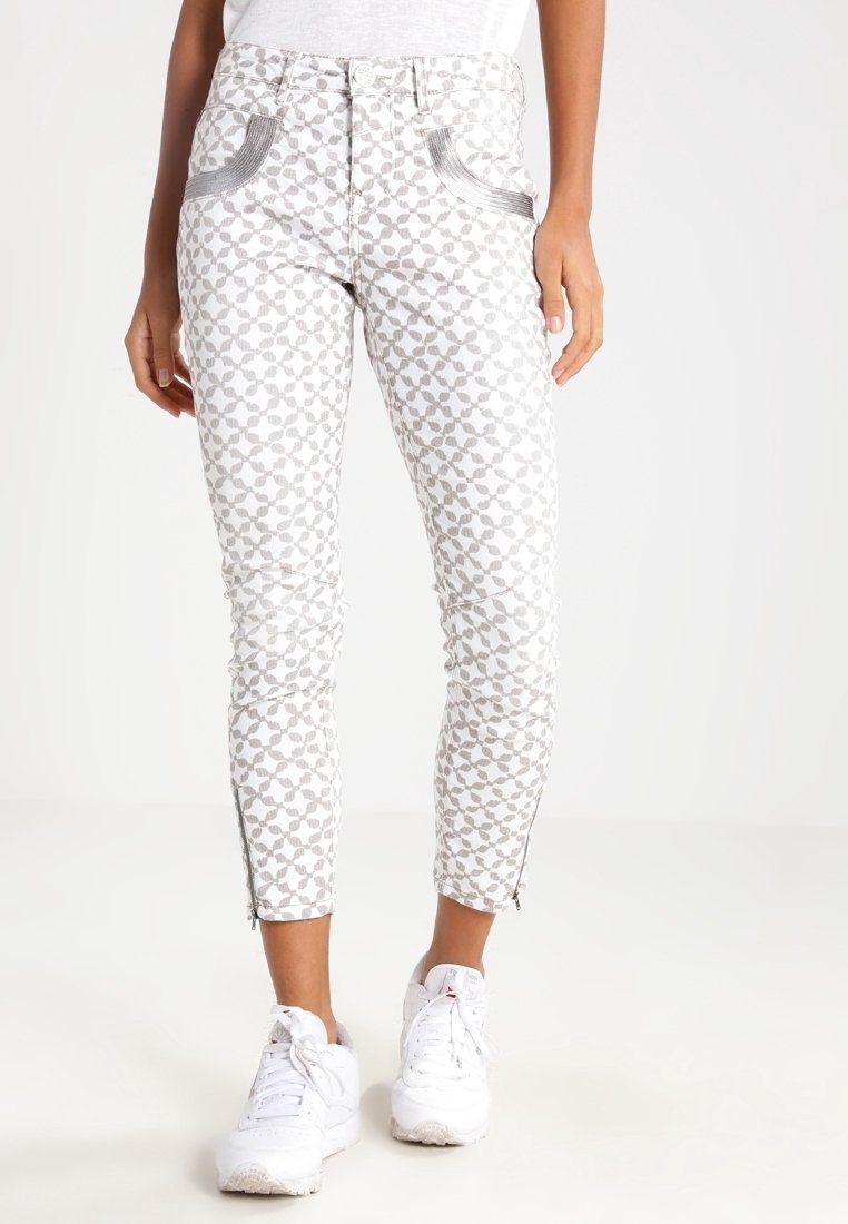 Pantalones blancos con un estampado de flores grises, que cuentan con cremalleras laterales, bolsillos angulados y un corte slim. Combinados con zapatillas blancas.