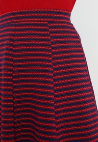 Punainen ja laivastonsininen kuviollinen hame, jossa on vaakasuoria raitoja ja teksturoitu pinta, varustettuna tiukalla vyötäröllä ja levenevällä muodolla.