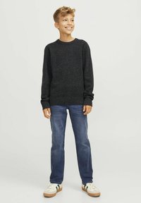 Pull en maille gris foncé à manches longues, avec des poignets et un ourlet côtelés, associé à un jean en denim bleu et des baskets beiges à rayures vertes.