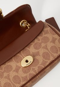 Brown crossbody bag featuring a patterned fabric exterior, smooth leather accents, and a gold-tone clasp with embossed logo detail.