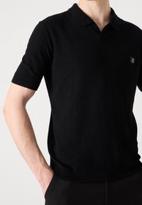 Zwarte polo met korte mouwen van een gestructureerde stof, V-hals ontwerp, ribgebreide manchetten en een klein logo op de borst.