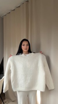 Weißer, oversized Pullover aus weichem, flauschigem Material mit Rundhalsausschnitt und geripptem Saum. Glatte Textur, minimales Design, keine sichtbaren Muster.