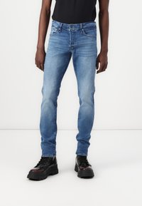 Jeanși din denim de culoare albastru deschis, cu o croială ajustată, având un design cu cinci buzunare și o ușoară decolorare. Asortați cu cizme negre cu șireturi.