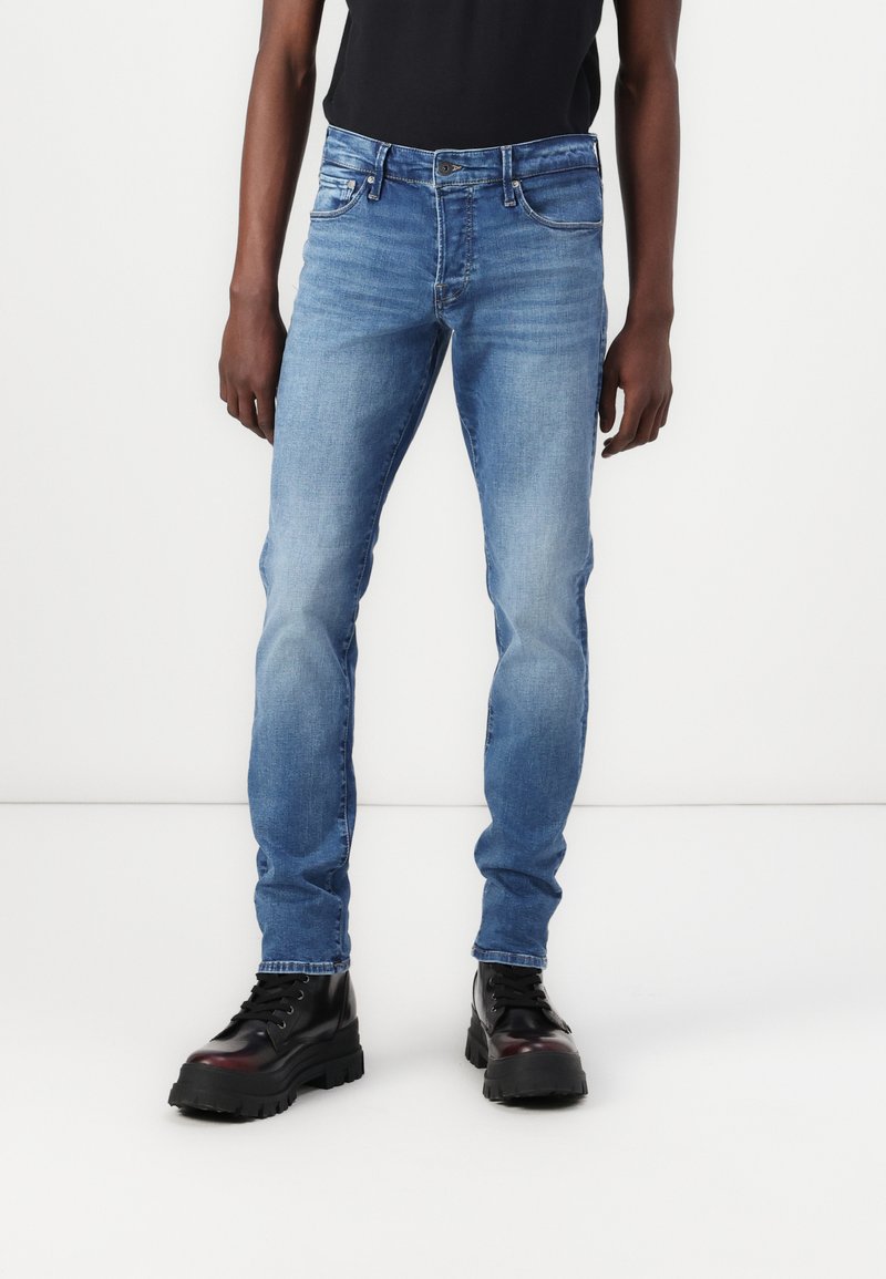 Jeanși din denim de culoare albastru deschis, cu o croială ajustată, având un design cu cinci buzunare și o ușoară decolorare. Asortați cu cizme negre cu șireturi.