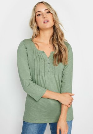 Haut vert à manches longues avec un décolleté en V, un design plissé et des accents de boutons. Tissu doux et texturé avec une coupe décontractée.