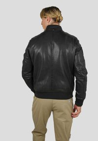 Veste aviateur en cuir noir avec poignets et ourlet côtelés, texture lisse et détails de couture subtils. Portée par une personne de dos.