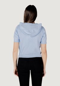 Sudadera de manga corta en un azul claro con un bolsillo tipo canguro en el frente, dobladillo acanalado y textura suave, combinada con pantalones ajustados negros.