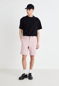 T-shirt noir à manches courtes, shorts roses avec poches avant, chaussures noires et chaussettes blanches. Design simple, tissu doux et coupe décontractée.