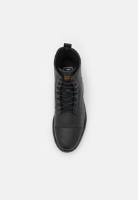 Černá kožená kotníková bota s hladkým povrchem, kulatou špičkou a šesti dírkami na šněrování. Obsahuje poutko vzadu a logem značky na bocích.