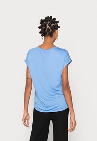 Světle modrý top s krátkými rukávy, volného střihu, měkké textury a zaobleným výstřihem, kombinovaný s černými žebrovanými kalhotami.