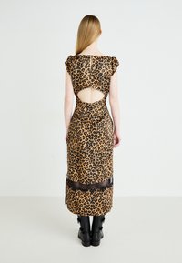 Robe midi à imprimé léopard avec de courtes manches bouffantes, détail de dos nu et bord en dentelle noire à l'ourlet. Associée avec des bottes noires à chevilles.