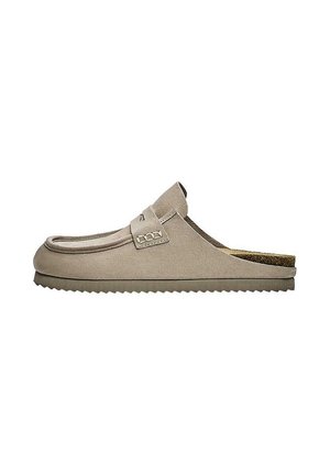 Beiger Slip-On Wildleder-Slipper mit flacher, geriffelter Sohle und dekorativem Riemen oben, von der Seite auf weißem Hintergrund gezeigt.