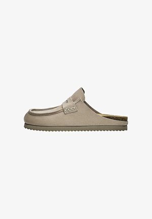 Mocassino beige in pelle scamosciata slip-on con suola piatta scanalata e cinturino decorativo nella parte superiore, visto di lato su sfondo bianco.