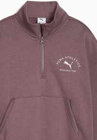 Bluza polarowa z półzamkiem w stonowanym fioletowym kolorze, wykonana z miękkiego materiału. Posiada przednią kieszeń kangura oraz haftowane logo Puma.