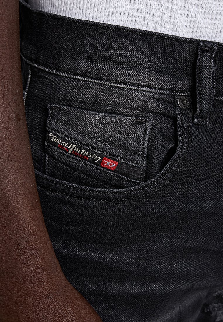 Schwarze Jeans aus Denim mit einer ausgewaschenen Textur, ausgestattet mit einer Gesäßtasche mit einem rot-weißen "Diesel Industry"-Etikett und kontrastierendem Stich.