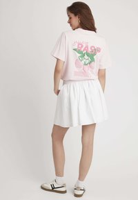 T-shirt graphique rose avec le texte "juicy RASP BERRY" et une illustration de framboise au dos, associé à une jupe évasée blanche et des baskets blanches.