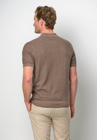 Brun kortärmad stickad polo med en strukturerad yta, med en platt krage och en figurnära siluett, kombinerad med ljusbeige byxor.