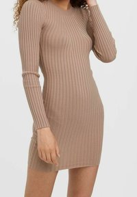 Ribbat jerseyklänning i ljusbrun, med långa ärmar och en figurnära silhuett som slutar ovanför knäna, och visar en texturerad tyg.