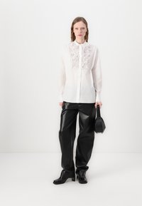 Chemise blanche à manches longues avec des détails floraux texturés à l'avant, associée à un pantalon en cuir noir brillant taille haute et un petit sac noir.