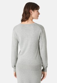 Světle šedý pletený svetr s dlouhými rukávy, žebrovanými manžetami a spodním lemem. Má kulatý výstřih a hladkou texturu. Zobrazeno ze zadní strany.