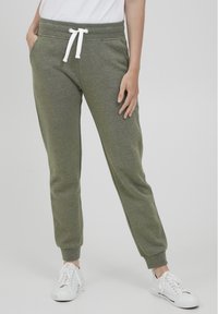 Olijfgroene joggers van zacht stof, met een witte trekkoord, zijzakken en taps toelopende benen met elastische boorden.