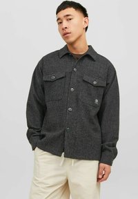 Camicia a quadri nera e grigia realizzata in tessuto testurizzato, con due tasche sul petto, chiusura con bottoni e colletto a punta.