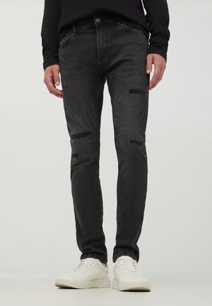 Jeans skinny neri con toppe strappate, realizzati in denim, con vita media e tasche anteriori, abbinati a sneaker bianche.