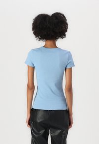 Camiseta corta de manga corta de rayas en azul claro con un diseño ajustado y escote redondo, combinada con pantalones negros brillantes y holgados.