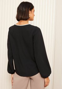 Blusa nera con maniche a sbuffo e scollatura rotonda, caratterizzata da un'accenno bianca lungo il colletto; tessuto liscio, leggero e vestibilità comoda.