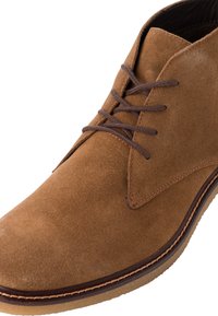Bottine chukka en daim marron avec des lacets marron et une texture douce, dotée d'une semelle en caoutchouc contrastante et d'accents cousus autour de la base.