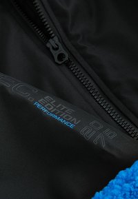Svart tyg med dragkedjestängning med blå text som säger "ELITE EDITION PERFORMANCE." Texturerat blått material i hörnet.