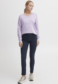 Világoslila, V nyakú pulóver sötétkék slim-fit nadrággal, bézs és szürke sportcipőkkel párosítva. A pulóver laza szabású és bordás mandzsettákkal rendelkezik.