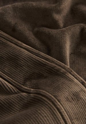 Brauner Stoff mit einer weichen, strukturierten Oberfläche, der sowohl glatte als auch gerippte Abschnitte aufweist. Das Material wirkt plüschig und langlebig.