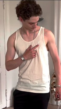 Beige Tanktop mit rundem Ausschnitt, figurbetontem Schnitt und kleinem Logo auf der Brust. Das Model trägt schwarze Hosen und eine silberne Uhr.
