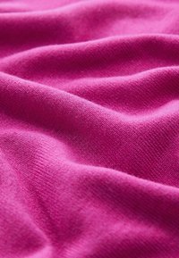 Tissu tricoté rose vif avec une texture douce, affichant des plis et des rides qui créent une apparence dynamique.
