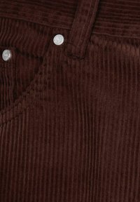 Pantaloni di velluto a coste marroni con texture a coste verticali, bottoni in metallo argentato e passanti per cintura standard. Vista ravvicinata dell'area della vita.