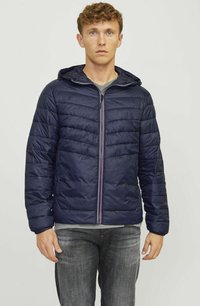 Chaqueta de plumas azul marino con cierre frontal, capucha y texturizado con acolchado en forma de chevrón. Presenta puños elásticos y un interior forrado. Llevada sobre una camiseta gris.