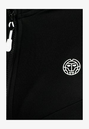 Schwarzer Stoff mit einem weißen Reißverschlussanhänger links und einem kleinen weißen runden Emblem mit einem stilisierten Gesicht rechts.