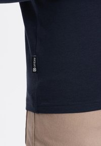 Tummansininen puuvillapaita lyhyillä hihoilla, jossa on sivustassa "ombre"-merkki ja sileä, istuva rakenne.