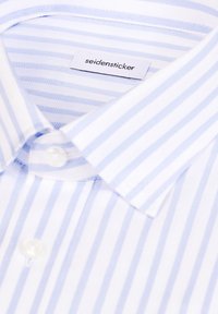 Gros plan sur le col d'une chemise rayée bleue et blanche avec des boutons blancs et une étiquette "seidensticker" à l'intérieur du col.