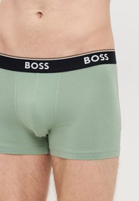 Boxers de algodão verdes com cintura preta, com a marca "BOSS" em branco, e um corte ajustado.