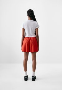Red shorts with an elastic waistband paired with a white short-sleeve T-shirt, viewed from the back. Black sneakers and white socks.