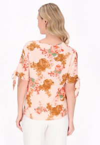 Blusa floreale rosa con un mix di grandi rose marroni e pesca, maniche corte con fiocchi e vestibilità rilassata. Tessuto dalla consistenza liscia.