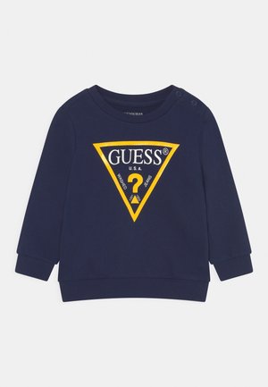 Marineblå langærmet sweatshirt til småbørn med gul trekantet GUESS-logo og trykknapper på skulderen.