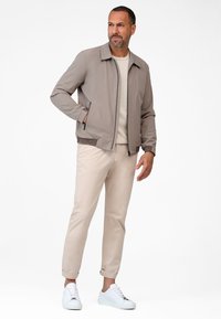 Light gray bomber jacket with a zip front, ribbed cuffs, and collar. Paired with beige pants and white sneakers. Simple, smooth texture.