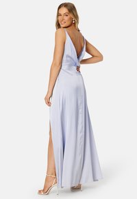 Abito in satin blu chiaro con schiena drappeggiata, spacco laterale e spalline sottili. L'abito presenta un design elegante e fluido, con una leggera lucentezza.